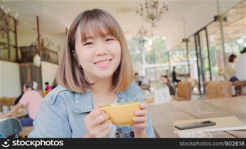 Business freelance Asian woman drinking warm cup of green tea or coffee while sitting on table in cafe. Lifestyle smart beautiful female relax in coffee shop concepts.
