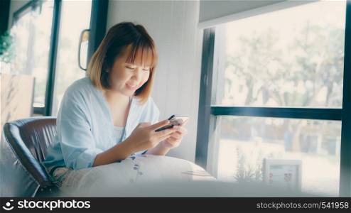 Business freelance Asian woman using smartphone for talking, reading and texting while sitting on table in cafe. Lifestyle smart beautiful women working at coffee shop concepts.