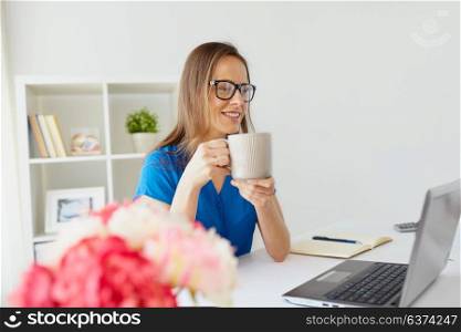 business, freelance, people and technology concept - happy smiling woman with laptop computer drinking coffee at home or office. woman with laptop and coffee at home or office