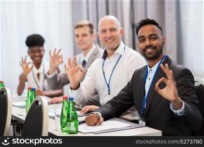 business, gesture and education concept - group of happy people at international conference showing ok hand sign. people at business conference showing ok hand sign