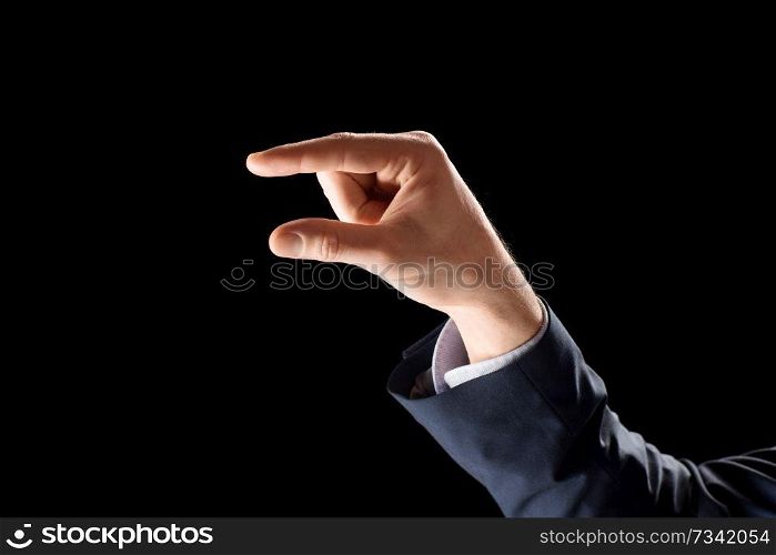 business, gesture and finger language concept - hand of businessman holding something imaginary or showing some small thing over black background. hand of businessman holding something imaginary