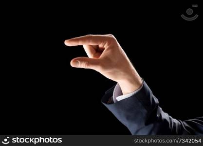 business, gesture and finger language concept - hand of businessman holding something imaginary or showing some small thing over black background. hand of businessman holding something imaginary