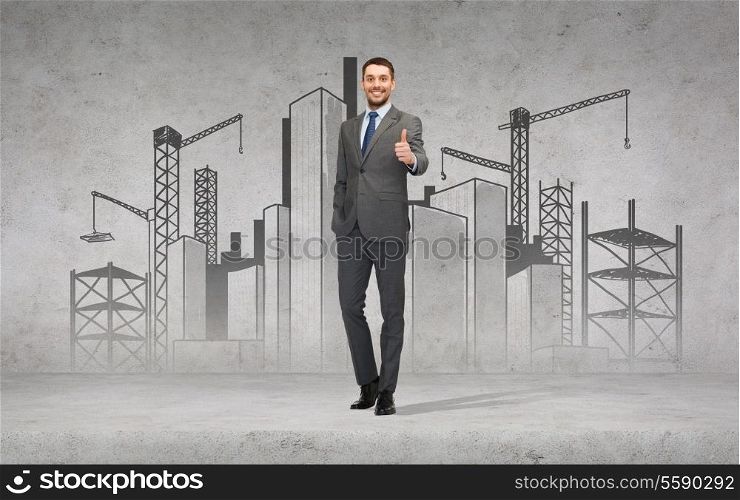 business, gesture and office concept - handsome businessman with construction site on the back showing thumbs up
