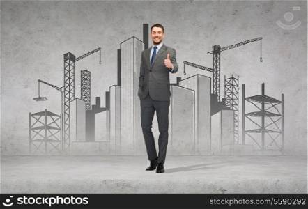 business, gesture and office concept - handsome businessman with construction site on the back showing thumbs up