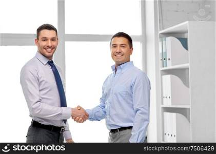 business, gesture and partnership concept - happy businessmen making handshake at office. happy businessmen making handshake at office