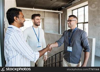 business, gesture and partnership concept - happy businessmen name tags making handshake at office. happy businessmen making handshake at office
