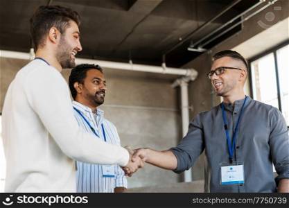 business, gesture and partnership concept - happy businessmen name tags making handshake at office. happy businessmen making handshake at office