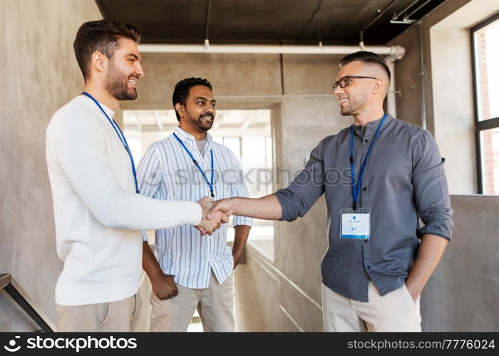 business, gesture and partnership concept - happy businessmen name tags making handshake at office. happy businessmen making handshake at office