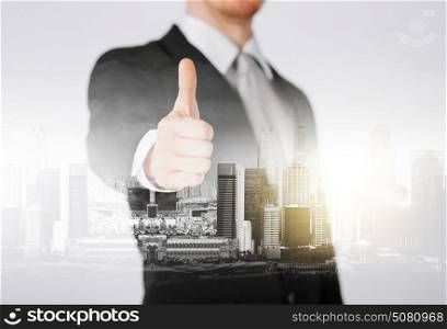 business, gesture and people concept - close up of businessman showing thumbs up over city with double exposure. businessman showing thumbs up