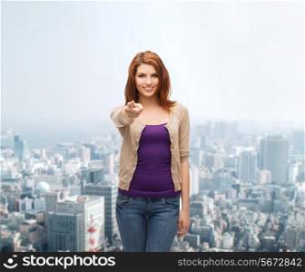 business, gesture and people concept - smiling teenage girl in casual clothes pointing finger on you over city background