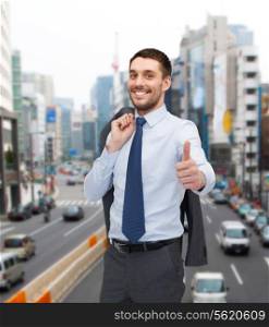 business, gesture and people concept - smiling young and handsome businessman showing thumbs up over cityscape background