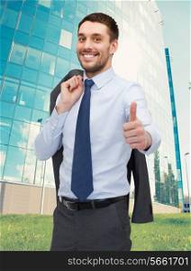 business, gesture and people concept - smiling young and handsome businessman showing thumbs up over business centre background