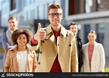 business, gesture and success concept - happy smiling man with international group of people showing thumbs up outdoors. happy smiling man showing thumbs up outdoors
