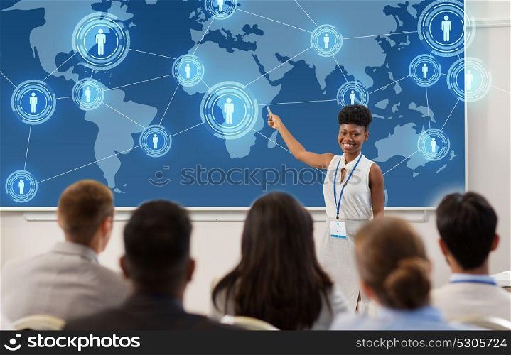 business, global network and people concept - smiling african american businesswoman or lecturer with world map on projection screen to group of students at conference presentation or lecture. group of people at business conference or lecture