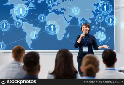 business, global network and people concept - smiling businesswoman or lecturer with world map on projection screen and microphone talking to group of students at conference presentation or lecture. group of people at business conference or lecture