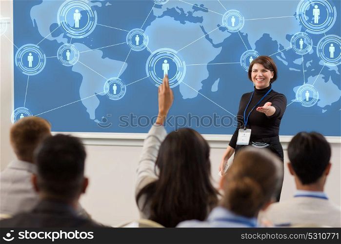 business, global network and people concept - smiling businesswoman or lecturer with world map on projection screen answering questions at conference presentation or lecture. group of people at business conference or lecture