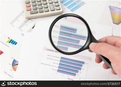 Business graph printed on the white paper with a hand holding a magnifier on it