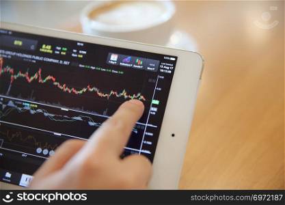 Business Hand Analyzing Stock finance Graph on Tablet with Coffee on wood background