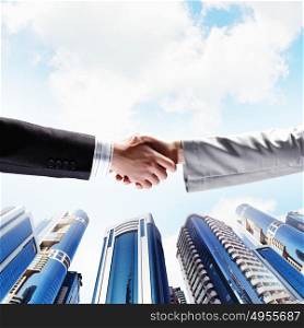 Business handshake. Close up image of hand shake against skyscrapers
