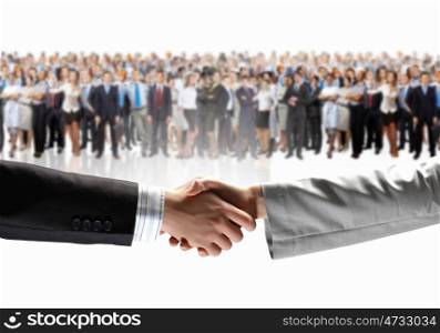 Business handshake. Close-up of human handshake with crowd of people at background