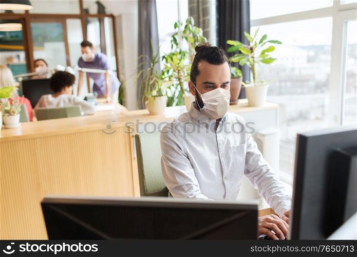 business, health and people concept - businessman or creative male office worker wearing face protective medical mask for protection from virus disease with computer. creative male office worker in mask with computer
