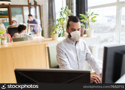 business, health and people concept - businessman or creative male office worker wearing face protective medical mask for protection from virus disease with computer. creative male office worker in mask with computer