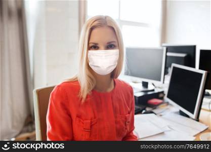 business, health and people concept - businesswoman or creative female office worker wearing face protective medical mask for protection from virus disease with computers. female office worker in mask with computers