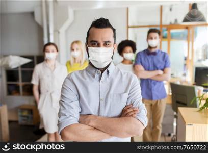 business, health and people concept - young man with beard over creative team wearing face protective medical mask for protection from virus disease at office. young man in mask over creative team in office