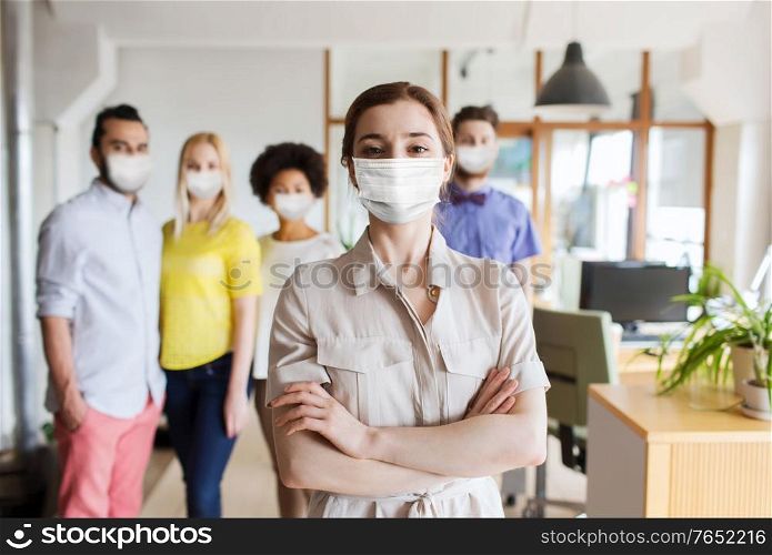 business, health and people concept - young woman over creative team wearing face protective medical mask for protection from virus disease at office. woman in mask over creative team at office