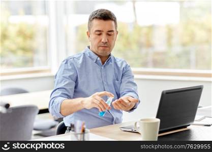 business, health care and pandemic concept - middle-aged man with laptop computer using antibacterial hand sanitizer at home office. man using hand sanitizer at home office