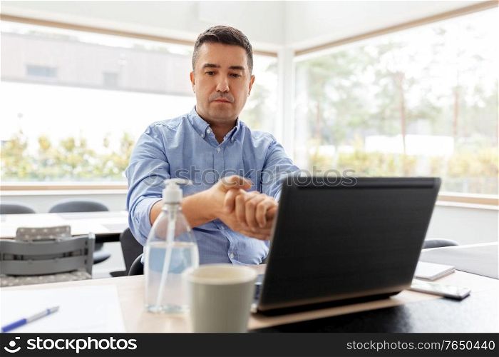 business, health care and pandemic concept - middle-aged man with laptop computer using antibacterial hand sanitizer at home office. man using hand sanitizer at home office