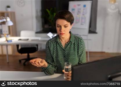 business, health problem and deadline concept - unhealthy businesswoman taking medicine pills at night office. businesswoman takes medicine pills at night office