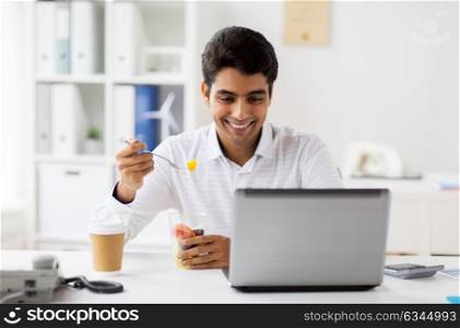 business, healthy eating and technology concept - businessman with laptop computer eating fruits at office meal break. businessman with laptop eating fruits at office