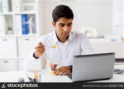 business, healthy eating and technology concept - businessman with laptop computer eating fruits at office meal break. businessman with laptop eating fruits at office