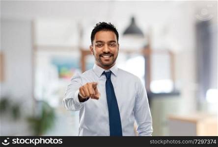 business, hiring and people concept - smiling indian businessman pointing to you in shirt with tie over office background. businessman pointing to you over office
