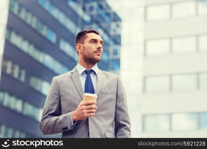 business, hot drinks and people and concept - young serious businessman with paper coffee cup over office building