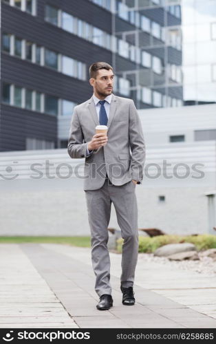 business, hot drinks and people and concept - young serious businessman with paper coffee cup over office building