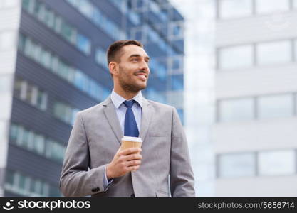 business, hot drinks and people and concept - young smiling businessman with paper coffee cup over office building