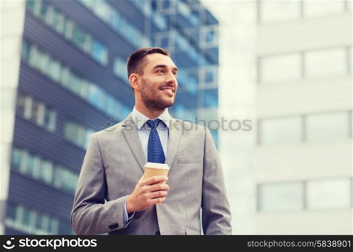 business, hot drinks and people and concept - young smiling businessman with paper coffee cup over office building