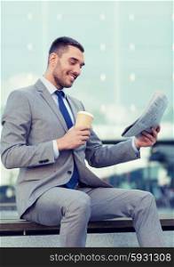 business, hot drinks and people and concept - young smiling businessman with paper coffee cup and newspaper over office building