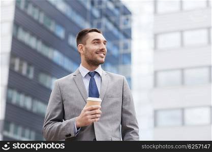 business, hot drinks and people and concept - young smiling businessman with paper coffee cup over office building
