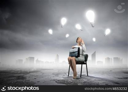 Business idea. Image of businesswoman sitting on chair with suitcase in hands