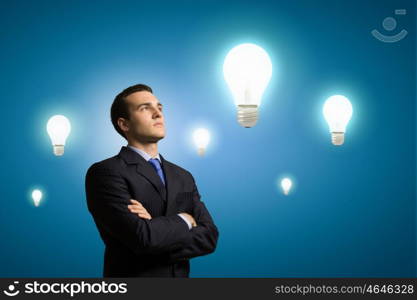 Business idea. Image of confident businessman with arms crossed looking at bulb. Idea concept