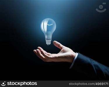 business, idea, inspiration and people concept - close up of businessman hand with light bulb over dark background. close up of businessman hand with light bulb