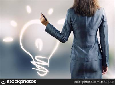 Business idea. Rear view of businesswoman drawing bulb with pen