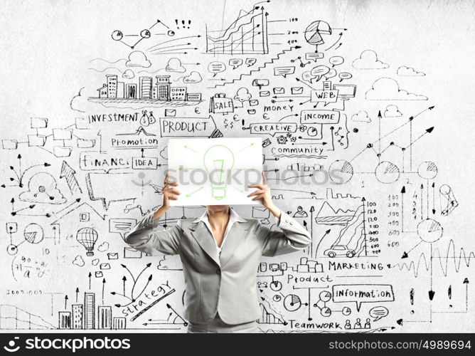 Business ideas. Businesswoman hiding her face with sheet of paper with sketches at background