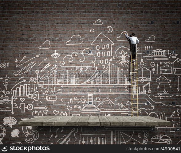 Business ideas on wall. Back view of businessman standing on ladder and drawing sketch on wall