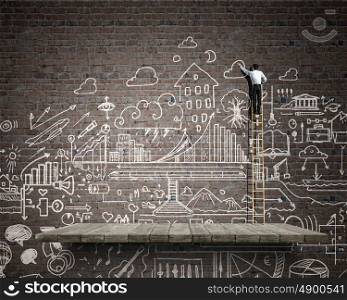 Business ideas on wall. Back view of businessman standing on ladder and drawing sketch on wall