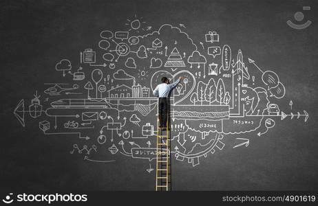 Business ideas on wall. Back view of businessman standing on ladder and drawing sketch on wall