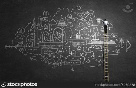 Business ideas on wall. Back view of businessman standing on ladder and drawing sketch on wall